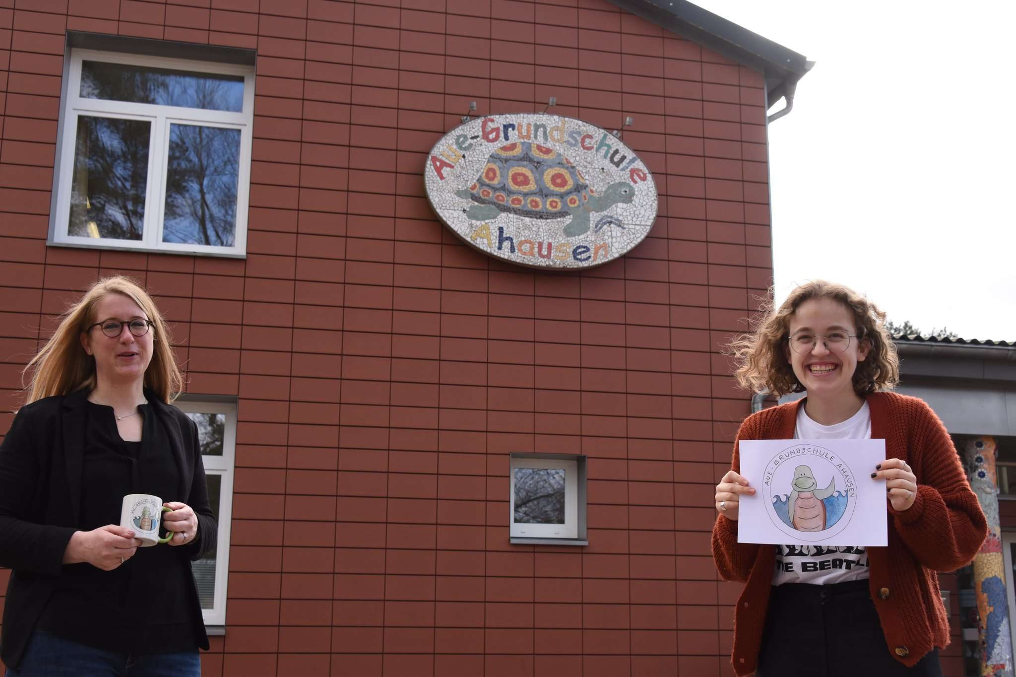 Nele Grabs (rechts) gestaltet das neue Logo für die Aue-Grundschule in Ahausen. Auch Schulleiterin Lavinia Wieland ist angetan von dem Werk, das auch auf den Tassen für die Erstklässler zu sehen ist. 